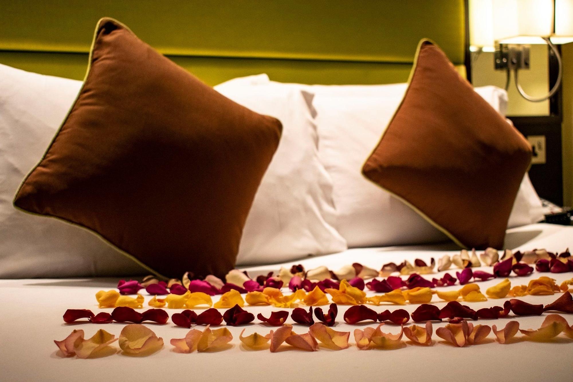 Montcalm Brewery Townhouse Hotell London Eksteriør bilde The photo shows a neatly arranged bed with two white pillows and brown decorative cushions. Scattered across the bed is a decorative display of flower petals in various colors, including pink, yellow, and orange, creating a romantic or tranquil ambia