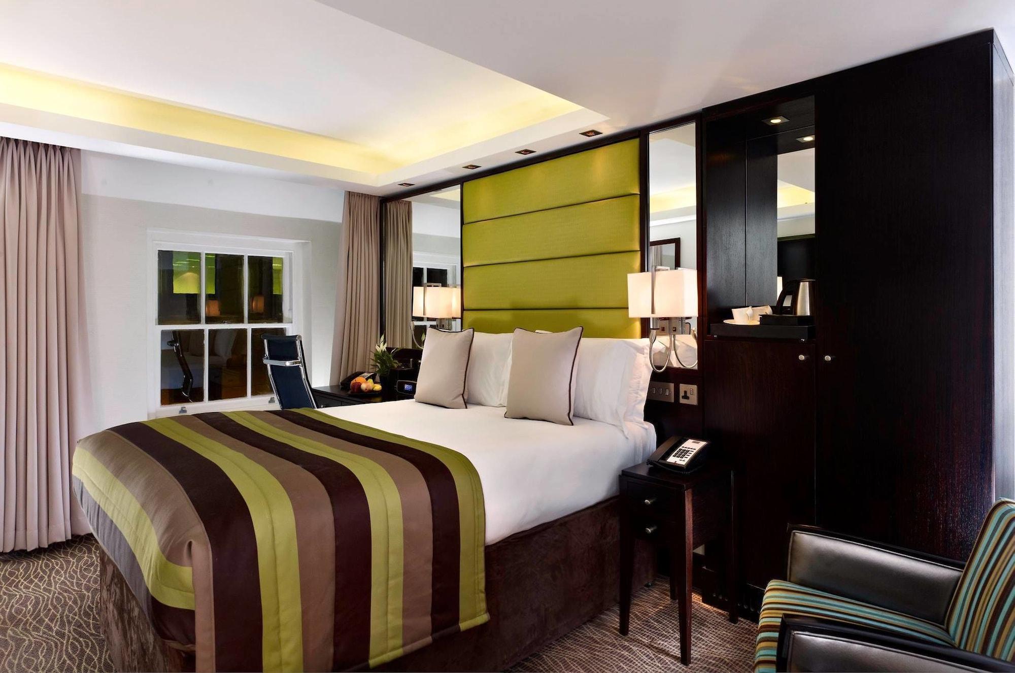 Montcalm Brewery Townhouse Hotell London Eksteriør bilde The photo shows a modern hotel room featuring a large bed with a striped comforter in shades of green, brown, and cream. The bed is adorned with several decorative pillows. Behind the bed, there is a contemporary headboard with a green panel design. 