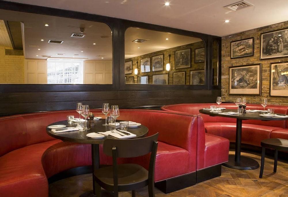 Montcalm Brewery Townhouse Hotell London Eksteriør bilde The image shows the interior of a restaurant featuring a warm and inviting atmosphere. There are several round tables surrounded by black chairs, with red, upholstered booths lining the walls. The decor includes framed artwork hanging on the walls, a