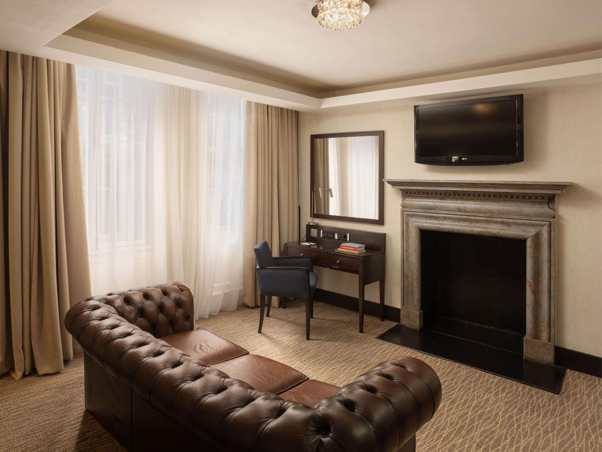 Montcalm Brewery Townhouse Hotell London Eksteriør bilde The photo shows a cozy and elegantly designed room. There is a comfortable brown leather sofa with tufted detailing. A small desk and chair are positioned near a mirror, providing a space for work or personal grooming. On the wall, a flat-screen TV i