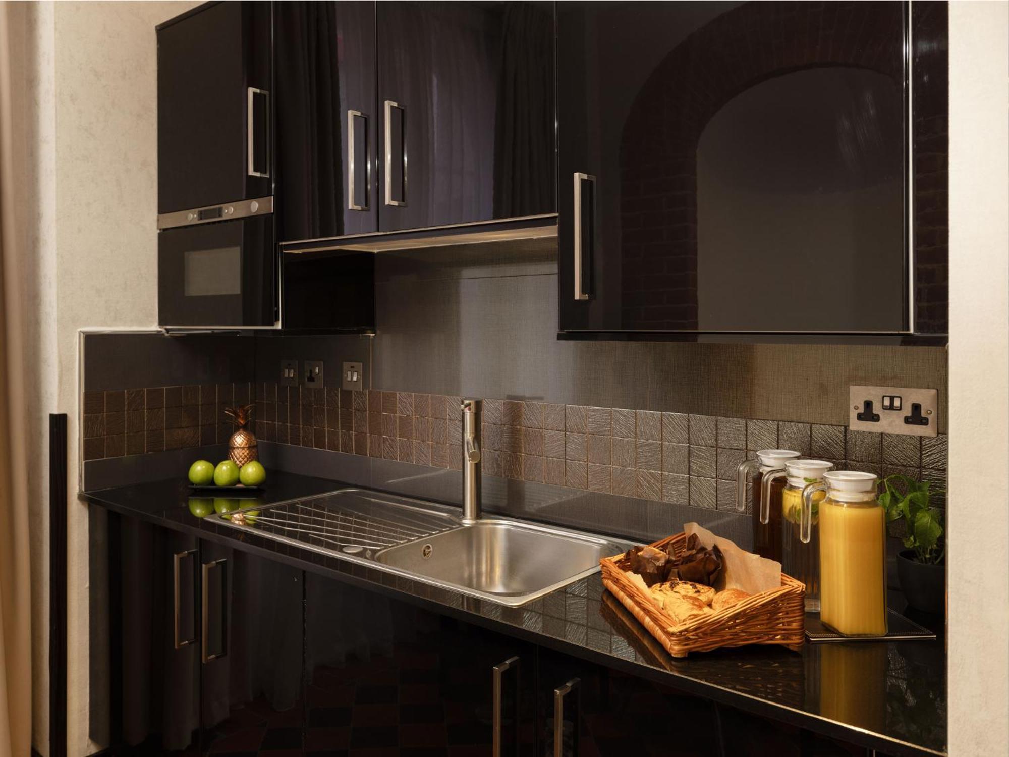 Montcalm Brewery Townhouse Hotell London Eksteriør bilde The photo shows a modern kitchen with sleek black cabinetry and a glossy finish. The kitchen features a stainless steel sink with a contemporary faucet, set against a dark, textured countertop. Above the counter, there are cabinets that match the cou