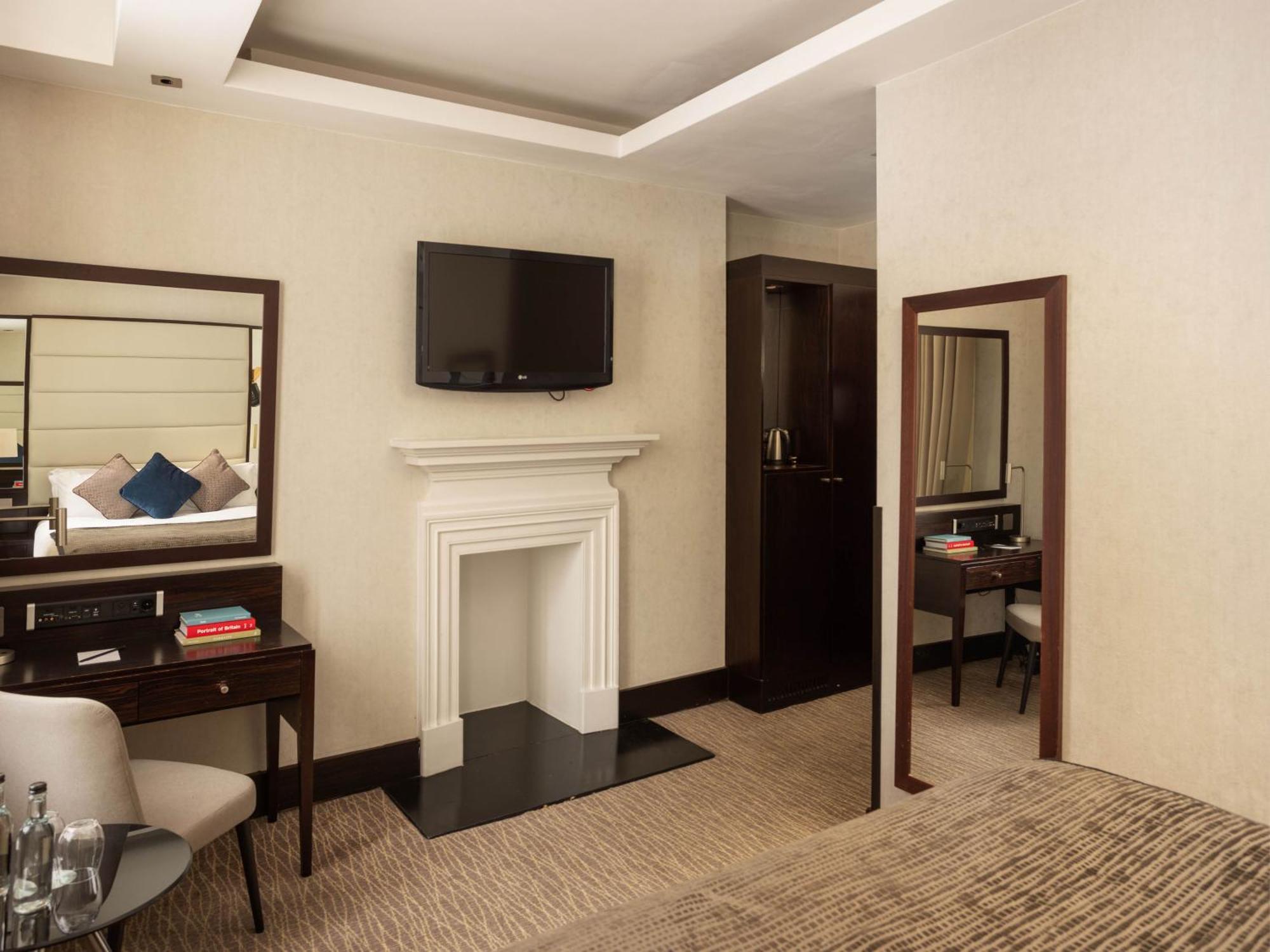 Montcalm Brewery Townhouse Hotell London Eksteriør bilde The photo depicts a stylish hotel room. It features a double bed, a large flat-screen TV mounted on the wall, and a decorative fireplace. There is a wooden desk with a chair beside it, as well as a mirror hanging on the wall. The decor is modern and 