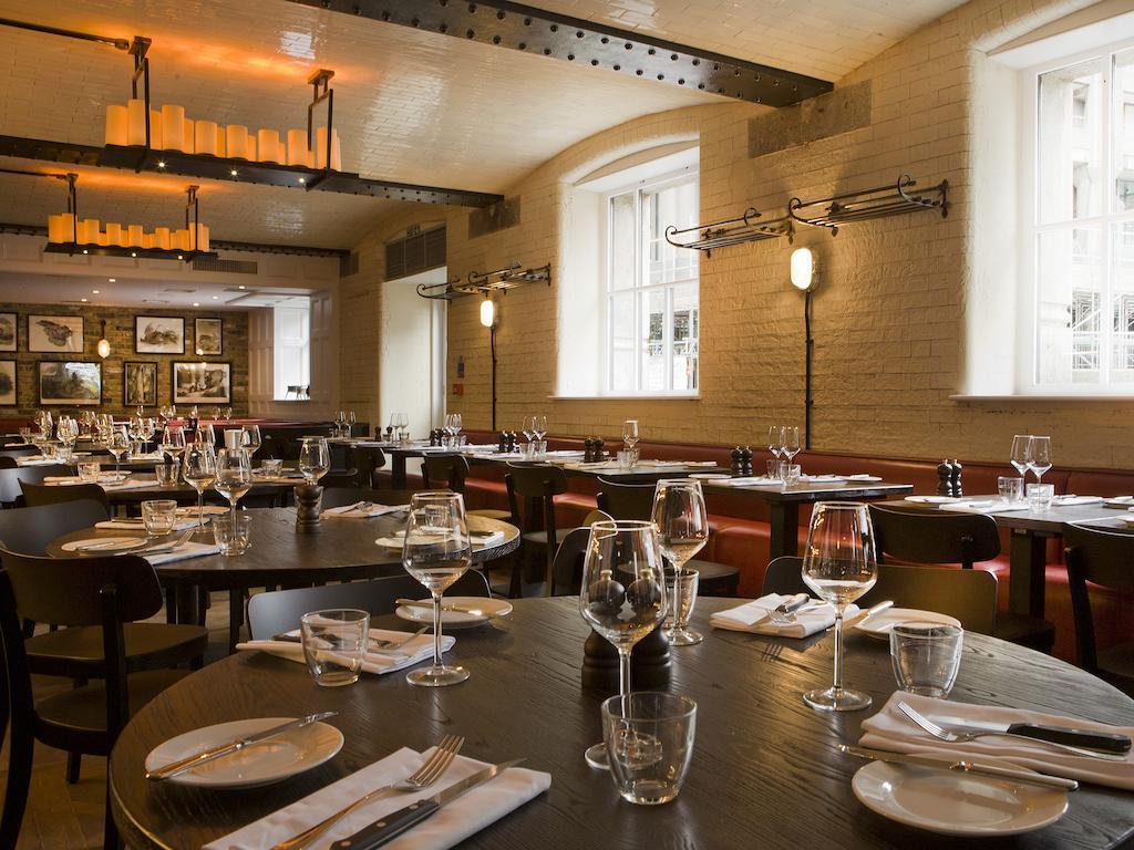 Montcalm Brewery Townhouse Hotell London Eksteriør bilde The photo shows a restaurant interior featuring a warm and inviting atmosphere. It has several round wooden tables set for dining, each with neatly arranged plates, utensils, and glasses. The lighting is soft, with overhead fixtures providing a cozy 