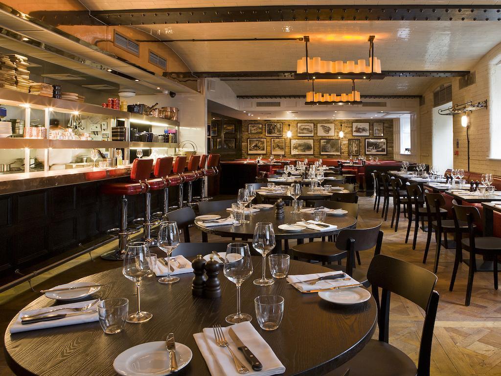 Montcalm Brewery Townhouse Hotell London Eksteriør bilde The photo shows the interior of a stylish restaurant. It features several round tables set with white plates, glasses, and silverware, all neatly arranged for dining. The decor includes a modern design with wooden floors and a mix of lighting fixture