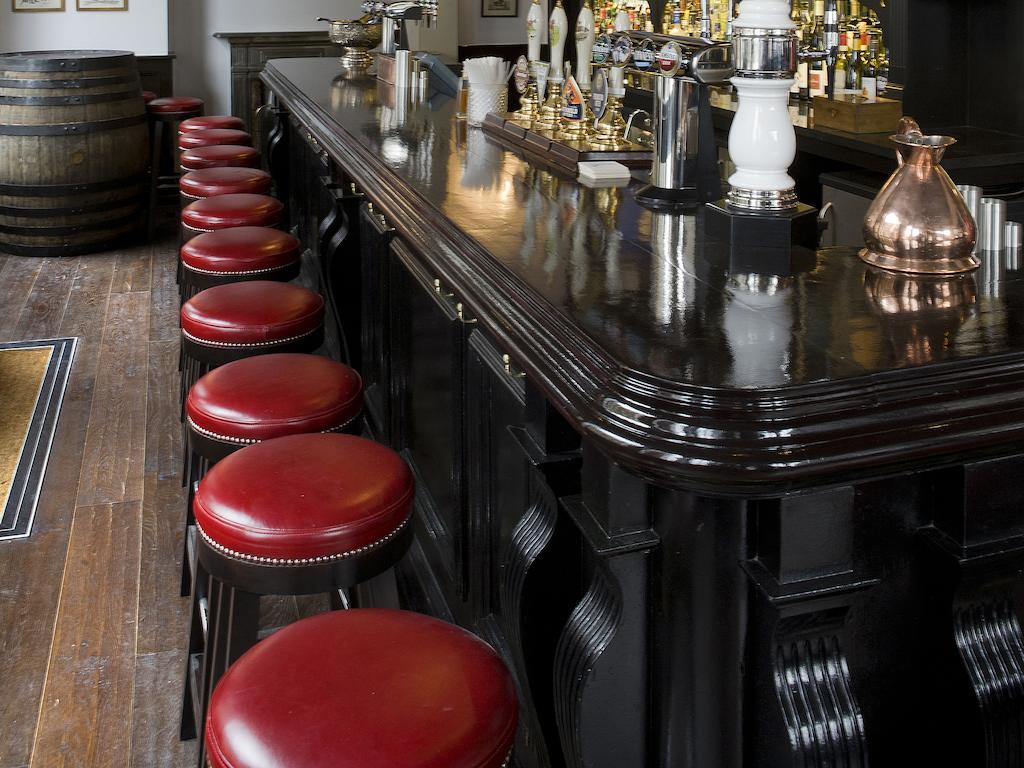Montcalm Brewery Townhouse Hotell London Eksteriør bilde The photo shows a bar setting with a long, polished dark wooden bar counter. Attached to the counter are several bar stools with red leather seats. Behind the bar, there are various bottles, suggesting a well-stocked bar. The flooring appears to be w