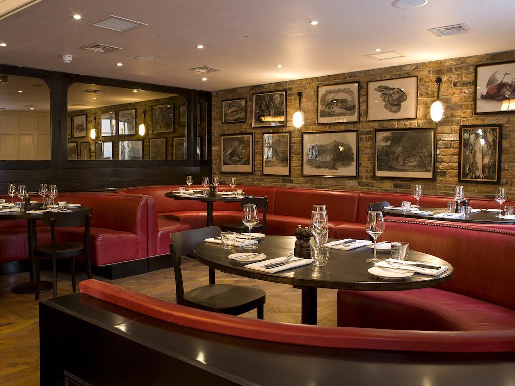 Montcalm Brewery Townhouse Hotell London Eksteriør bilde The photo depicts an elegant restaurant interior. There are curved red booths along the walls, creating a cozy seating arrangement. The tables are round and set with white plates and glassware, indicating a prepared dining area. The walls feature a n